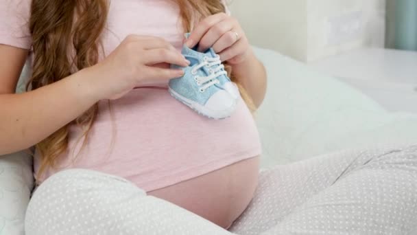 CPrimo piano della donna incinta che si sveglia sulla pancia grande con stivali o scarpe per bambini piccoli. Concetto di gravidanza e attesa del bambino — Video Stock