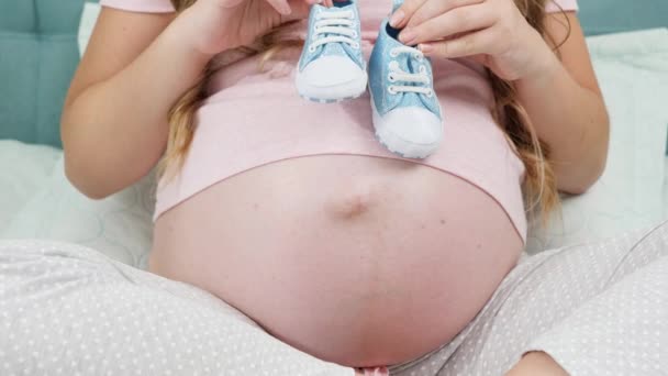 Closeup έγκυος γυναίκα περιμένει το αγοράκι κρατώντας μικρές μπότες μωρό στα χέρια. Έννοια της εγκυμοσύνης και αναμένοντας το μωρό — Αρχείο Βίντεο