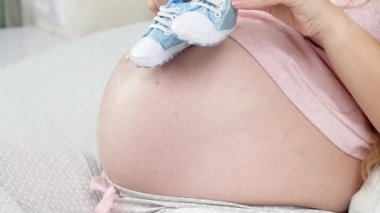 Koca göbeğinde Newbon bebekleri için ayakkabı tutan hamile kadının yakın çekimi. Hamilelik kavramı, bebek hazırlamak ve doğurmak