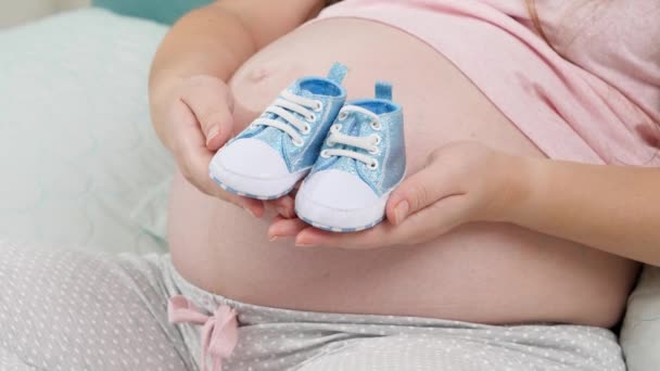 Primer plano de la fiesta del bebé. Mujer embarazada esperando a bebé niño sosteniendo botas azules recién nacidas en las manos — Vídeo de stock