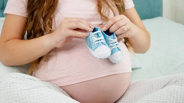 CLoseup av gravid kvinna vakna på stor mage med små barn stövlar eller skor. Begreppet graviditet och väntar barn — Stockfoto
