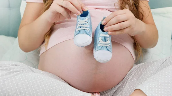 CLoseup de la mujer embarazada que espera al niño sosteniendo pequeñas botas de bebé en las manos. Concepto de embarazo y embarazo — Foto de Stock