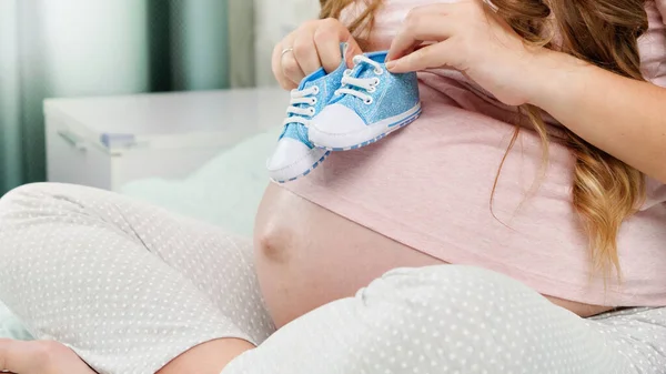 CLoseup av gravid ung kvinna går runt hennes stora mage med små stövlar för nyfödda barn — Stockfoto