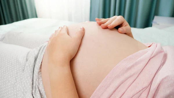 Detailní záběr těhotné ženy hladící a dotýkající se jejího nenarozeného dítěte pohybujícího se a bijícího ve velkém břiše. Koncepce těhotenství, příprava a očekávání dítěte — Stock fotografie