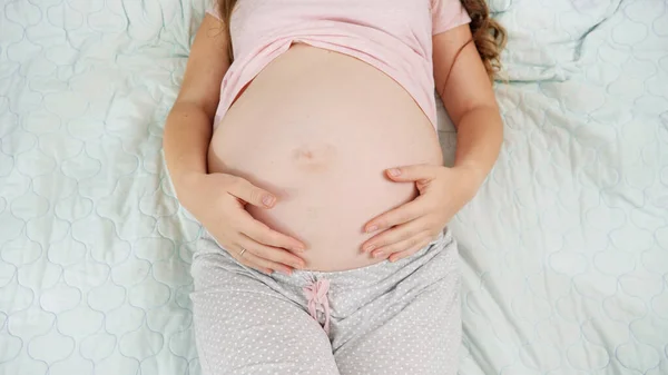 Draufsicht einer schwangeren Frau, die auf dem Krankenhausbett liegt und ihren dicken Bauch berührt und streichelt. Konzept der Schwangerschaft, Vorbereitung und Schwangerschaft. — Stockfoto