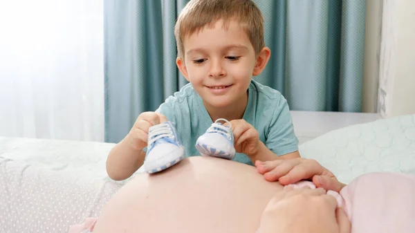 Zbliżenie z starszy syn chodzenie z dziecko buty akroos Duży brzuch w ciąży matka leżąca na łóżko w sypialni — Zdjęcie stockowe