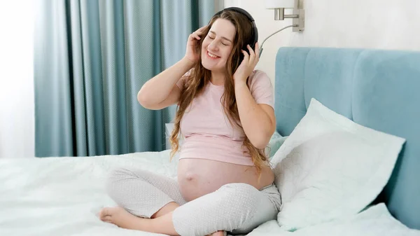 大きな腹を持つ幸せな笑顔妊娠中の女性はヘッドフォンで音楽を聞くことを楽しんでいます.生まれていない赤ん坊は母親の腹部にいる間クラシック音楽を聞いている。初期の芸術と創造性の発展の概念 — ストック写真