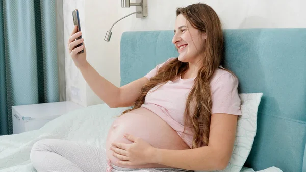 Retrato de feliz sorrindo mulher grávida tendo conversa em vídeo ou conferência no smartphone. — Fotografia de Stock
