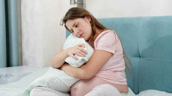 Zwangere vrouw die op bed zit en een groot kussen knuffelt. Concept van maternale en zwangerschapsdepressie. — Stockfoto