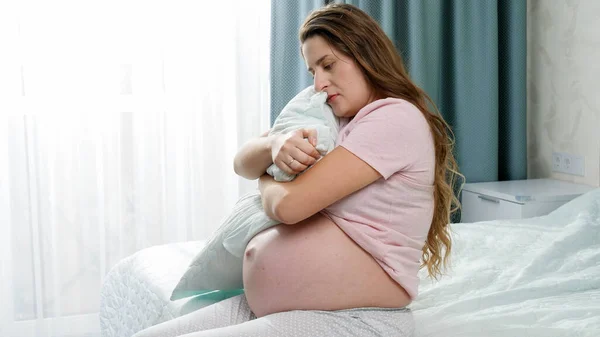 Üzgün, hamile bir kadın büyük bir yastık tutuyor ve yatakta oturuyor. Annelik ve hamilelik depresyonu kavramı. — Stok fotoğraf