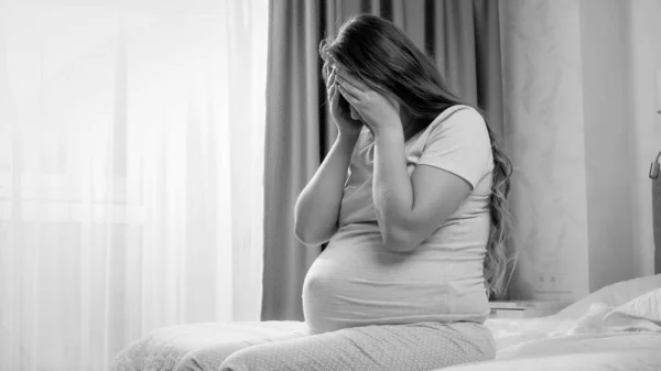 Black and white image of young pregnant woman suffering from depression crying on bed. Concept of maternal and pregnancy depression — Stock Photo, Image