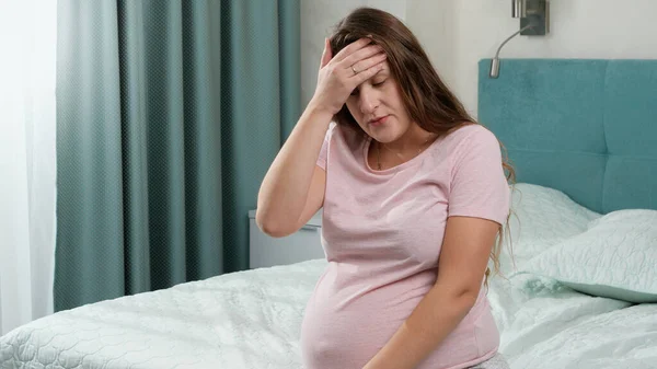 Porträtt av upprörd gravid kvinna känner sig ensam och upprörd sitter på sängen hemma. Begreppet moderns och graviditetens depression. — Stockfoto