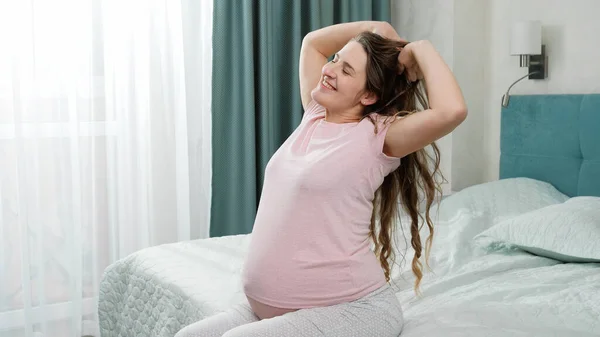 Retrato de una feliz mujer embarazada sonriente en pijama estirándose en la cama por la mañana después de despertarse. Concepto de felicidad durante el embarazo y el embarazo — Foto de Stock