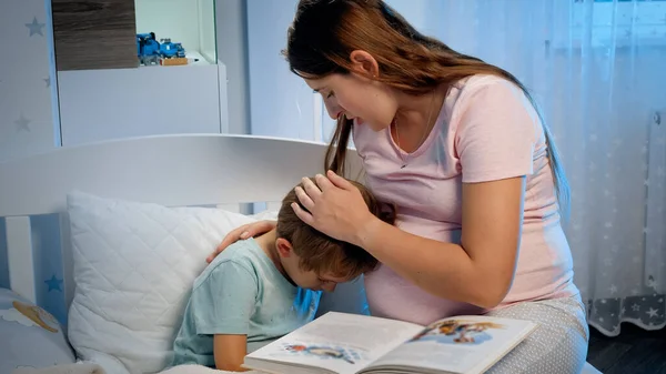 Jovem mãe grávida abraçando e acalmando seu menino chorando deitado na cama à noite. Cuidados e amoroso pai abraçando criança — Fotografia de Stock