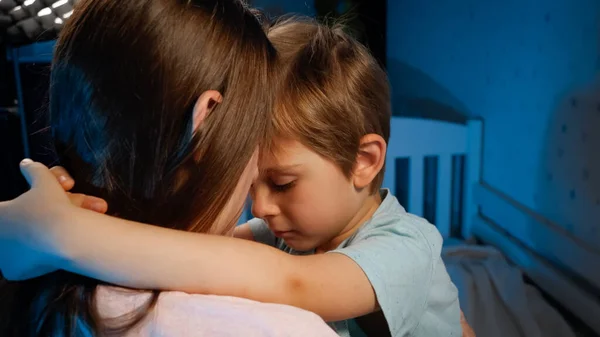 Retrato de um menino pequeno e triste abraçando e beijando sua mãe antes de ir dormir à noite. Amorosos e carinhosos pais e filhos — Fotografia de Stock