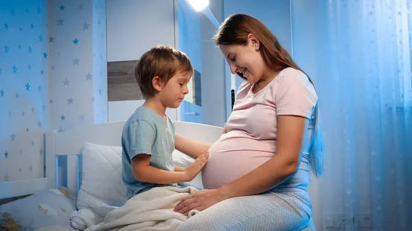 小さな幼児男の子ストロークと愛撫大腹の彼の妊娠中の母親前に夜にベッドに行く — ストック写真