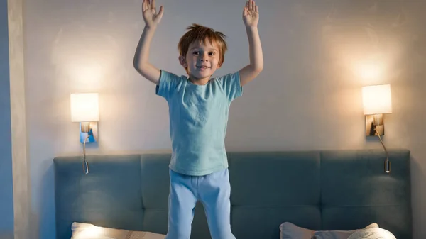 Engraçado menino de pijama pulando e dançando na cama dos pais à noite. Menino da criança sem dormir e ativo antes de ir dormir — Fotografia de Stock