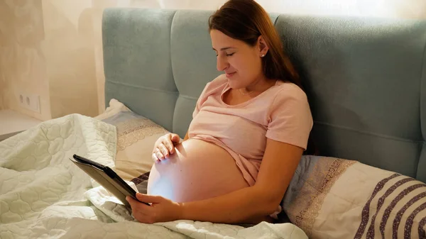 Retrato de jovem grávida com barriga grande deitada na cama com computador tablet e internet de navegação — Fotografia de Stock