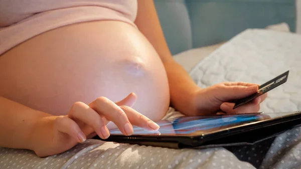 Close-up de mulheres grávidas navegando na internet em tablet segurando cartão de crédito. Mulher esperando bebê fazendo compras on-line e compra de roupas online — Fotografia de Stock