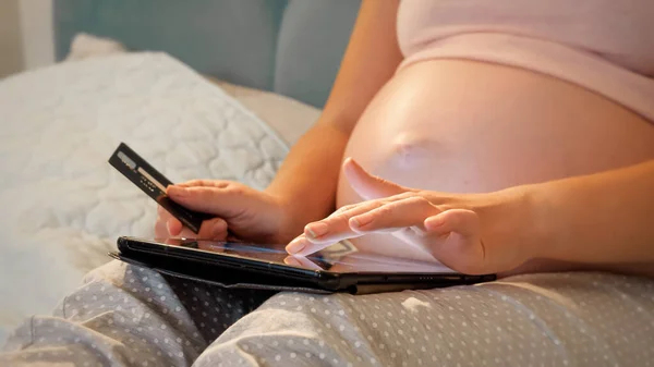 임신 한 여성이 큰 배에 신용 카드를 들고 온라인 쇼핑을 할 때 태블릿 컴퓨터를 사용하는 모습이 목격되었습니다. 온라인 쇼핑과 전자 상품권의 개념 — 스톡 사진