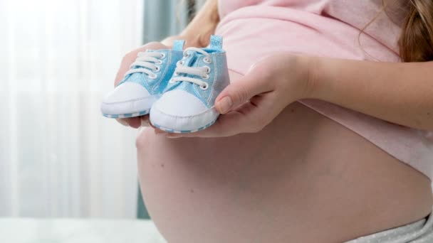 Primer plano de las pequeñas botas de bebé recién nacidas azules en las manos de yougn mujer embarazada — Vídeo de stock