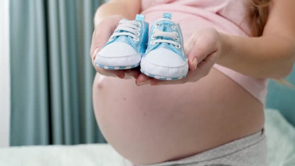 Närbild av vacker gravid kvinna med stor mage väntar på baby pojke hålla små stövlar på händerna — Stockvideo