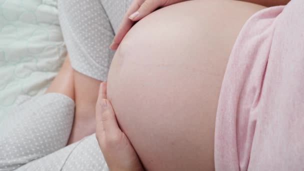 임산부가 앉아서 큰 배를 부드럽게 쓰다듬는 모습이 눈에 띈다. 출산, 임신 및 건강 관리에 대한 개념. — 비디오