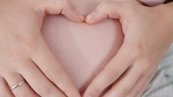 임신부가 손을 큰 배에 얹고 손가락으로 심장 모양을 만드는 장면을 확대 해 보라. 아이, 사랑, 양육에 대한 개념. — 비디오