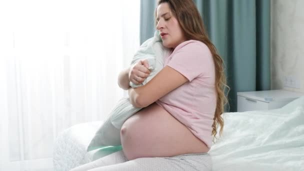 Droevige jonge zwangere vrouw met een groot kussen en zittend op bed. Concept van maternale en zwangerschapsdepressie. — Stockvideo