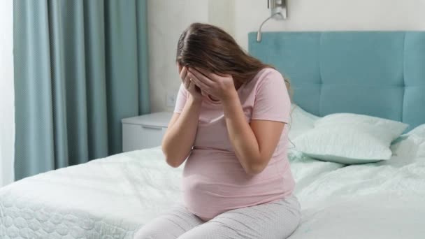 Droevig huilende zwangere vrouw die lijdt aan depressie zittend op bed en haar hoofd vasthoudend. Concept van maternale en zwangerschapsdepressie. — Stockvideo