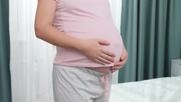 Ztráta těhotné ženy dotýkat a hladit její velké břicho vedle velkého okna v ložnici. Koncept štěstí během těhotenství a očekávání dítěte — Stock video