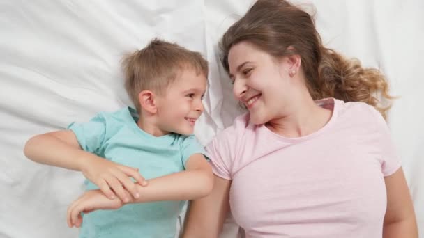 Retrato de vista superior do menino bonito deitado com a jovem mãe na cama e falando. Conceito de parentalidade e felicidade familiar — Vídeo de Stock