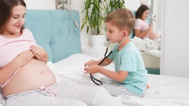 Malý batole chlapec předstírající, že je doktor pomocí stetoskopu poslouchat srdeční sázku svého nenarozeného bratra ve velkém břiše těhotné matky. Koncepce zdravotní péče a lékařské prohlídky během těhotenství — Stock video