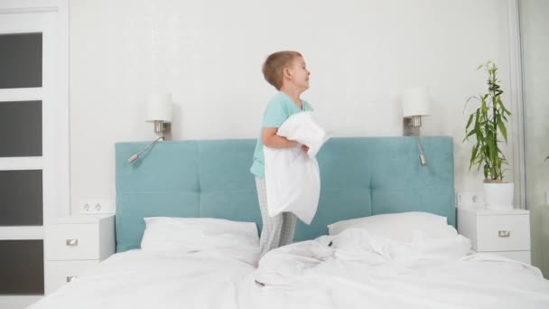 Slow motion van vrolijke peuter jongen houden kussen en springen hoog op bed bij ouders slaapkamer. Concept van gelukkige kinderen in het weekend — Stockvideo