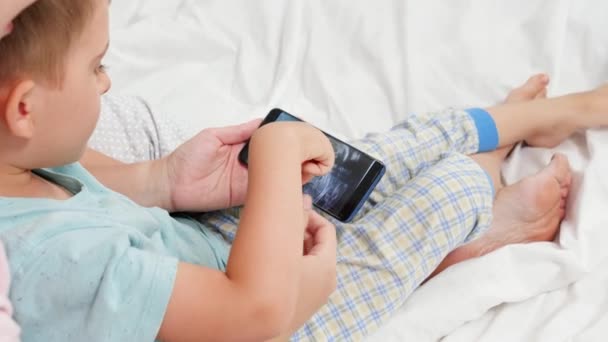 Großaufnahme eines kleinen Jungen, der das Ultraschallbild seines ungeborenen Bruders auf dem Smartphone der Mutter betrachtet. Konzept der Gesundheitsfürsorge und des Familienglücks — Stockvideo