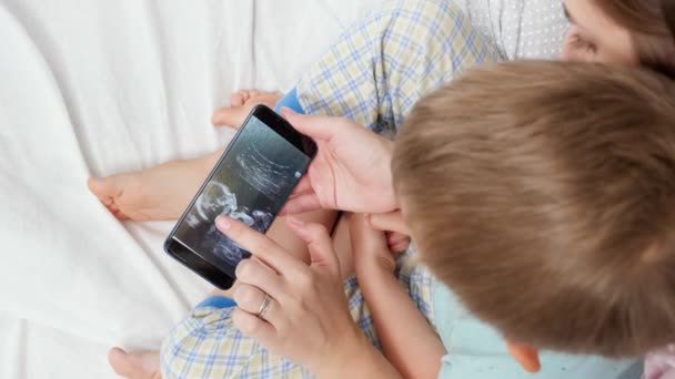 Primo piano del bambino con giovane madre incinta che guarda l'immagine ecografica del futuro bambino. Concetto di assistenza sanitaria e felicità familiare in attesa del bambino — Video Stock