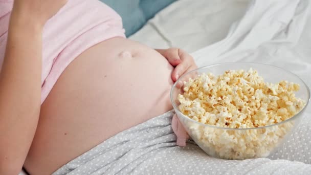 Detailní záběr těhotné ženy v pyžamu relaxaci v posteli a jíst popcorn při sledování televize — Stock video