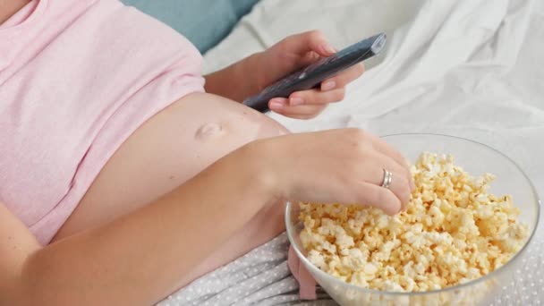 Detailní záběr těhotné mladé ženy sledování televize v posteli a jíst popcorn z velké misky — Stock video