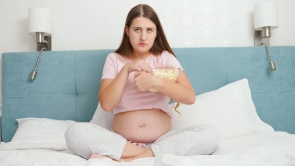 Mujer embarazada concentrada viendo películas en la televisión y comiendo palomitas de maíz de un tazón grande — Vídeos de Stock