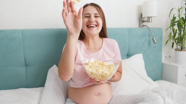 SLow pohyb veselé těhotné ženy držící misku popcornu a házející ji do kamery. Těhotná žena se baví a cítí šťastný — Stock video