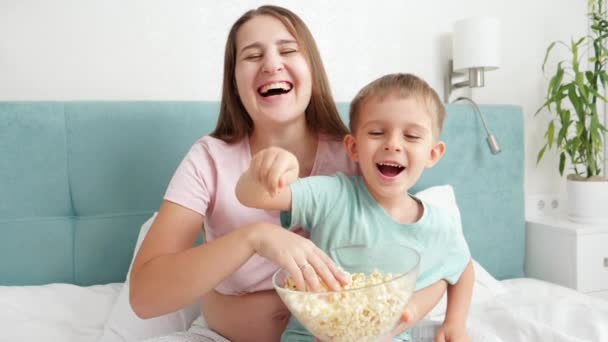 Slow motion van vrolijke kleine jongen met moeder gooien popcorn uit grote kom in de camera. Familie heeft plezier en voelt zich gelukkig — Stockvideo