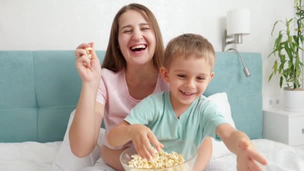 Χαρούμενο γελαστό αγοράκι με νεαρή μητέρα να βλέπει ταινίες στην τηλεόραση και να πετάει ποπ κορν στην κάμερα. Η οικογένεια διασκεδάζει και νιώθει ευτυχισμένοι μαζί. — Αρχείο Βίντεο