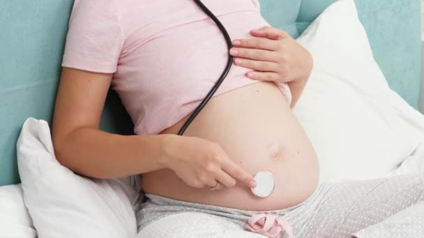 CLoseup de mulher grávida usando stetschope e segurando-o em sua barriga grande com o feto. Conceito de cuidados de saúde e exame médico durante a gravidez — Vídeo de Stock