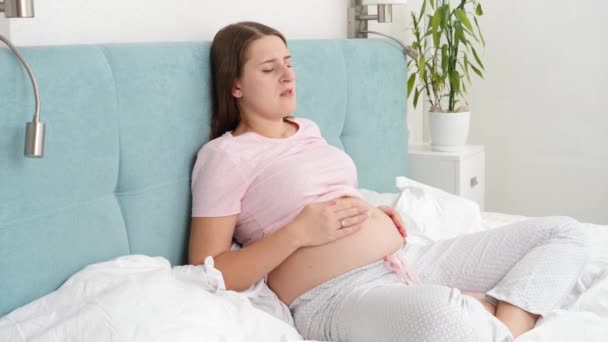 Jeune femme enceinte ressentant une douleur dans le ventre reposant au lit et caressant son ventre. Soins de santé et intoxication pendant la grossesse — Video