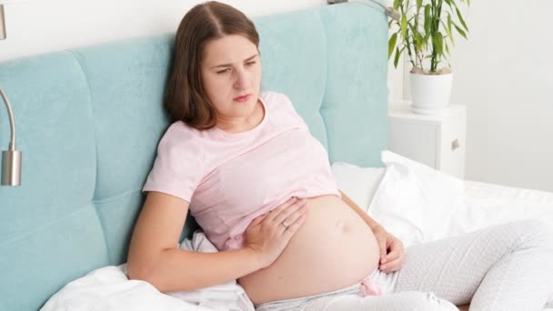 Jeune femme enceinte ressentant une douleur intense dans l'estomac tenant les mains sur le ventre alors qu'elle était couchée au lit à la maison — Video