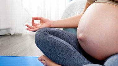 Genç hamile kadın derin nefes alıyor ve evde yoga yaparken lotus pozitinde oturuyor. Hamilelik boyunca sağlıklı yaşam tarzı, sağlık ve spor kavramı
