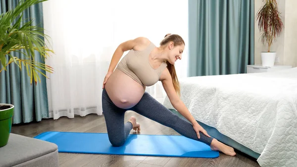 Giovane donna incinta sorridente che si allunga e si riscalda prima di fare fitness a casa. Concetto di assistenza sanitaria e sport durante la gravidanza. — Foto Stock