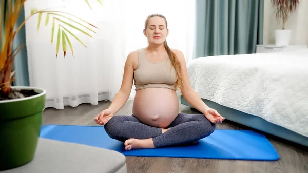 Bella donna incinta sorridente praticare yoga seduto su fitness pazzo in posa loto e respirare profondamente. Concetto di assistenza sanitaria e sport durante la gravidanza — Foto Stock