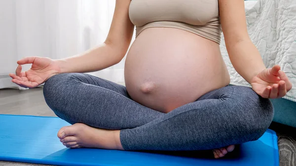 Jonge zwangere vrouw met grote buik zittend op fitness mat en mediterend thuis. Concept van gezonde levensstijl, gezondheidszorg en sport tijdens de zwangerschap — Stockfoto