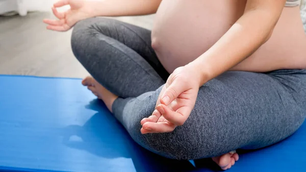 CPrimo piano di donna incinta piegando le dita e seduto in posa loto yoga sul tappeto fitness a grande finestra. Concetto di stile di vita sano, assistenza sanitaria e sport durante la gravidanza — Foto Stock